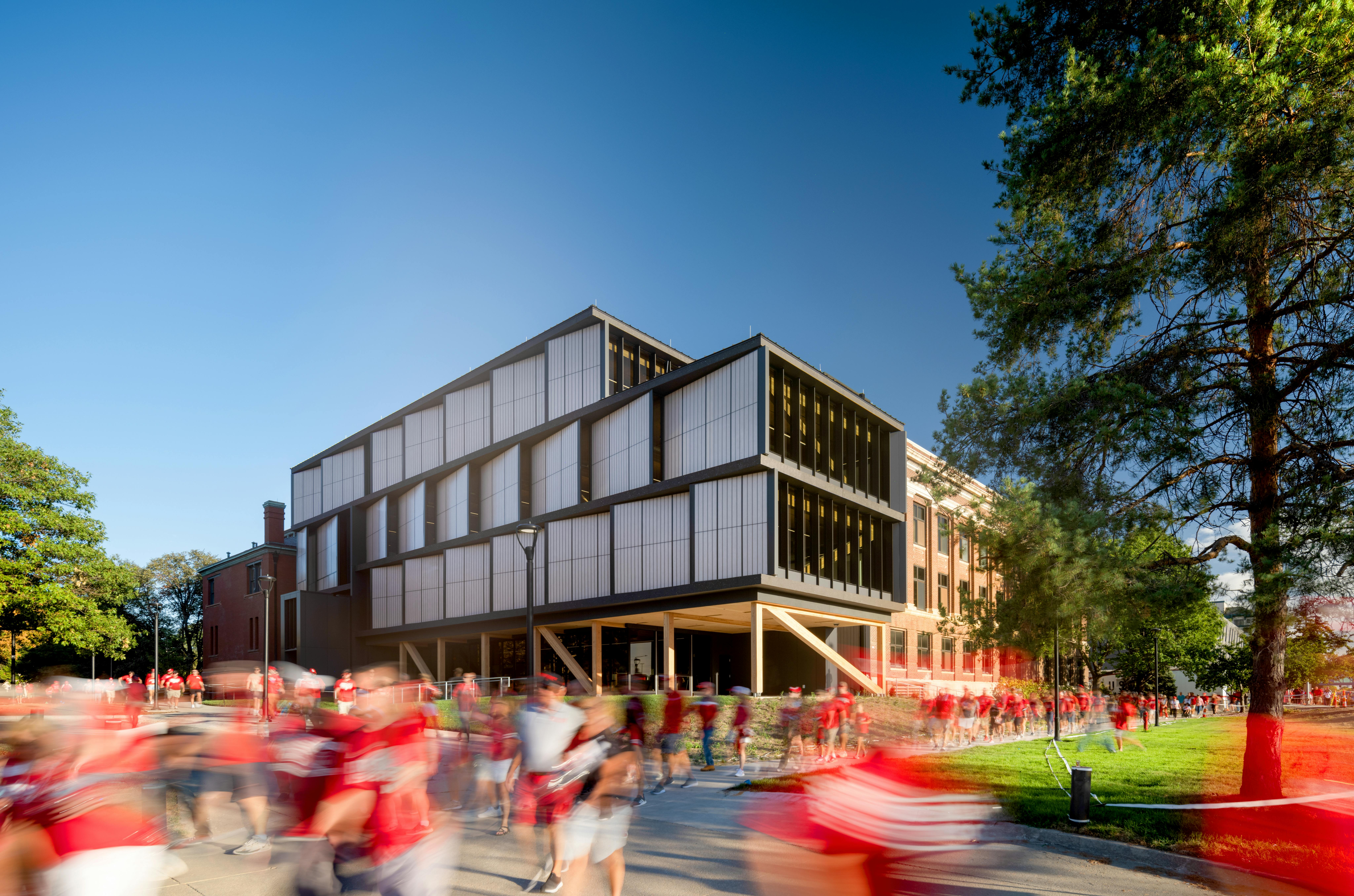 The mass timber and metal addition to the north facade of UNL's historic Architecture Hall was designed to be a material complement to the original red brick, hip-roofed, timber structure, visible here in the background.