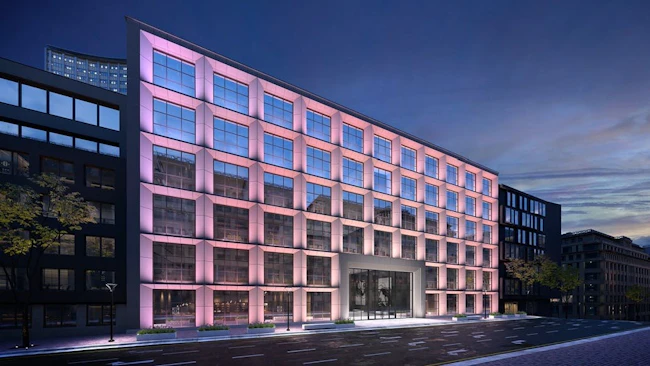 Building facade with exterior lights in soft purples, pinks, yellows, and white.