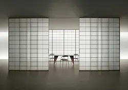 Sliding door system made from translucent panels with gridded aluminum pattern reveal partial view of conference table and chairs inside the room.