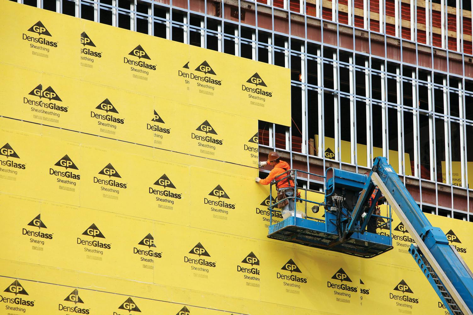 Installation of DensGlass Sheathing, rows of gold-finished fiberglass mats on structural frame.