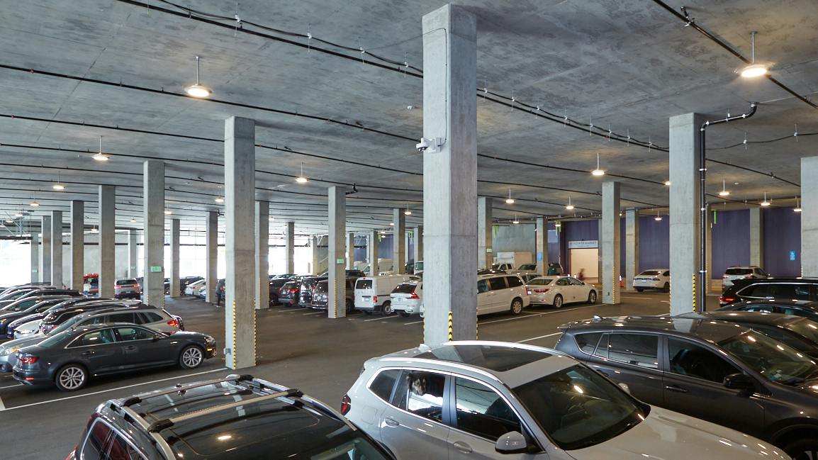 Interior of a parking garage showing cars, concrete beams, and SensScape SPG18 parking luminaires.